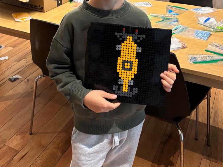 Pol sujetando un tablero negro con un diseño suyo en dots amarillos, sobre la mesa donde prepara los kits